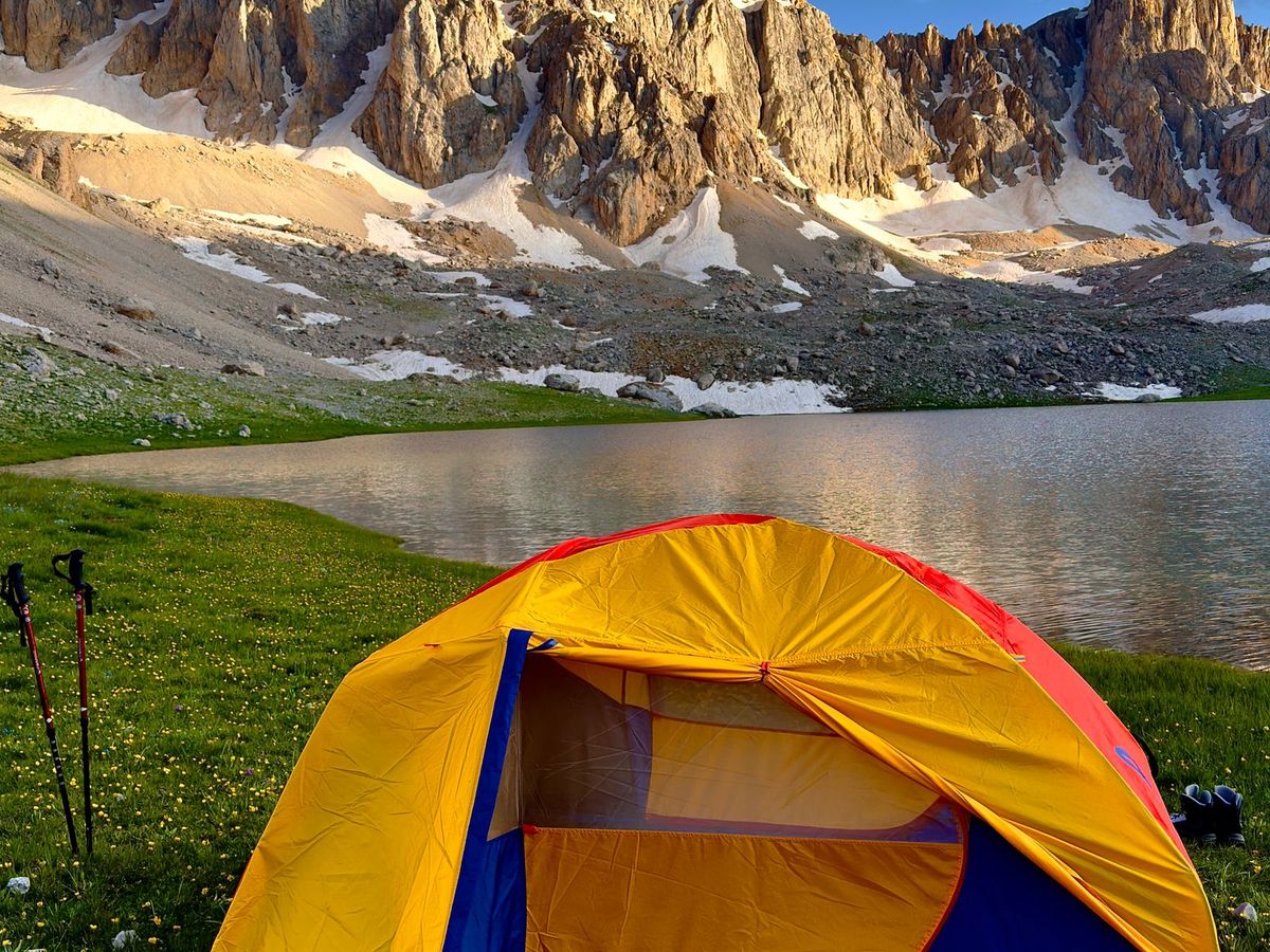A tent beside a mountain lake at sunset — the classic thru-hiking camp