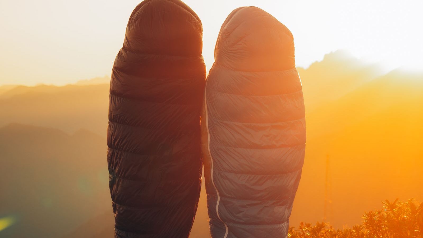 Two campers in sleeping bags inside a tent at sunrise