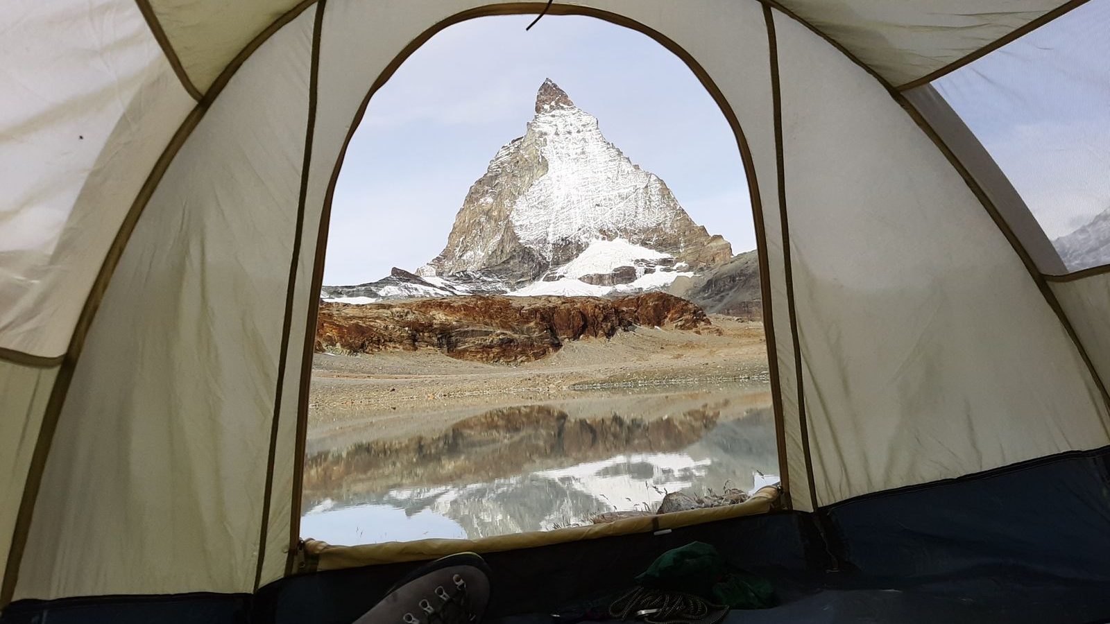 View from inside a tent, lying on a sleeping pad, looking out at a mountain peak and lake