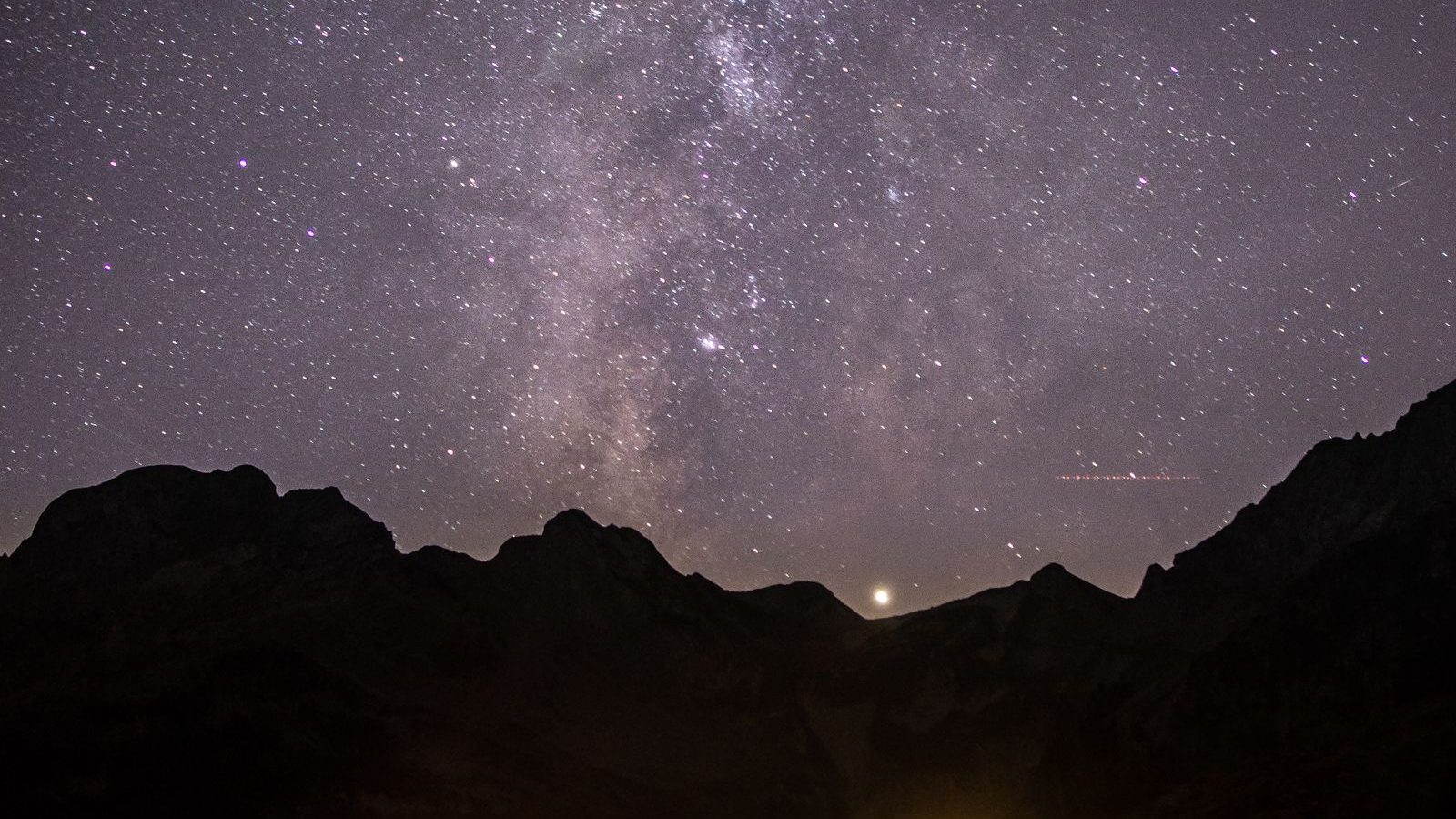 A camper lying on their side by a bonfire and tent under a starry sky