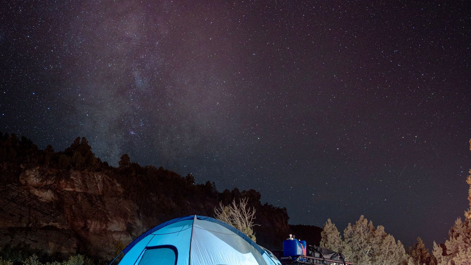 A blue dome tent under a starry night sky in the desert mountains