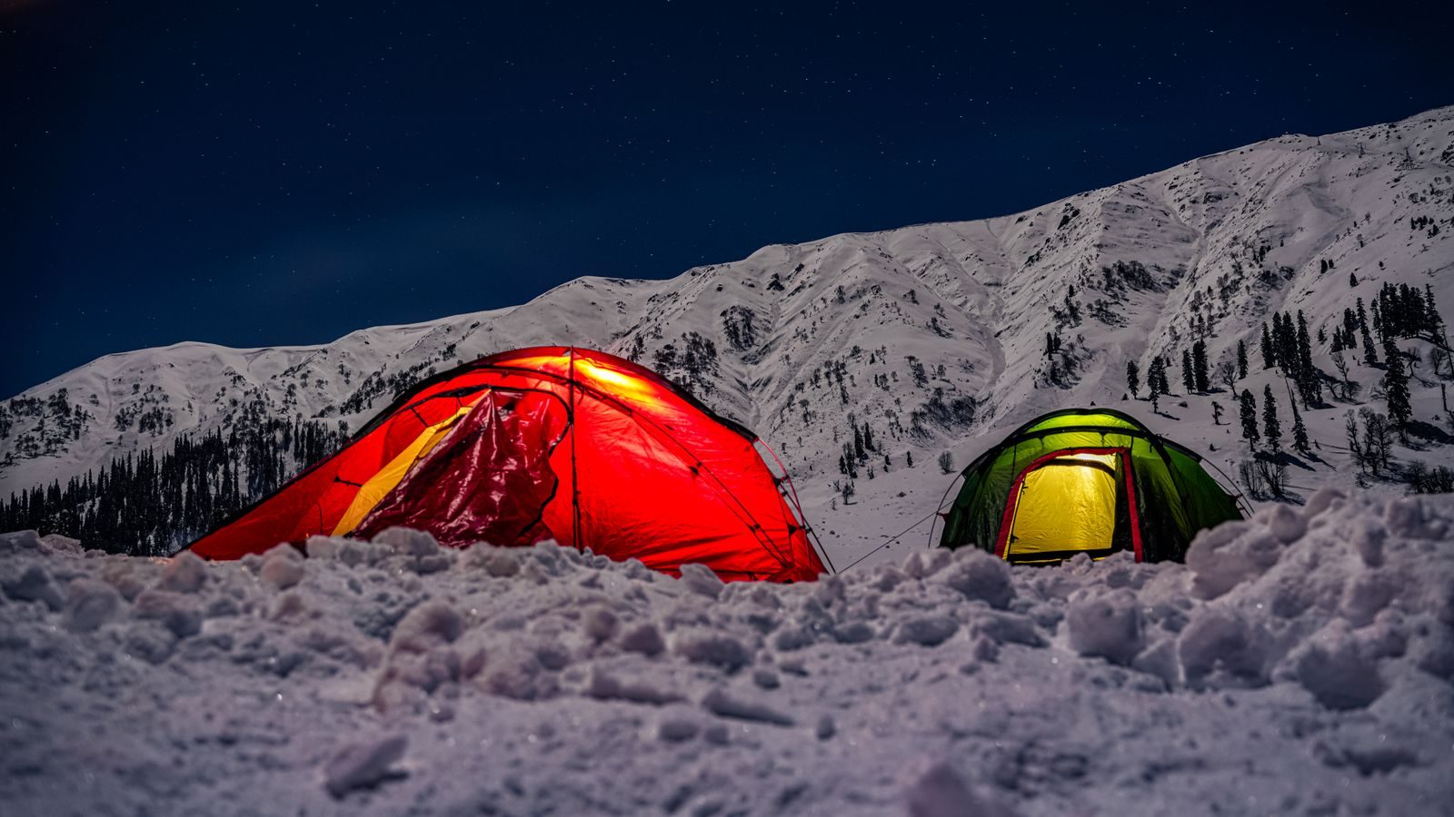 Two illuminated tents on a snowy mountain slope under a starry night sky