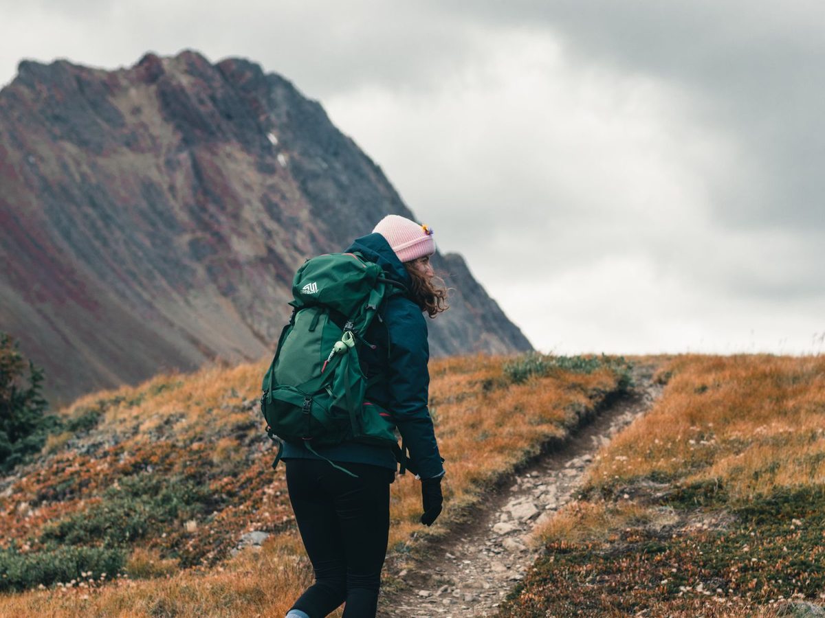 A woman with a backpack climbing on a mountain trail