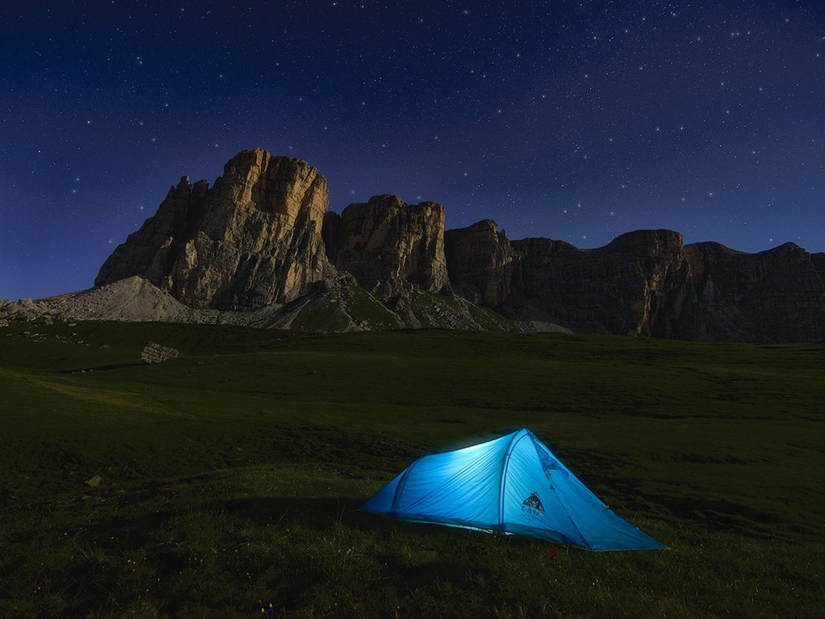 A blue dome tent pitched near a mountain in alpine country