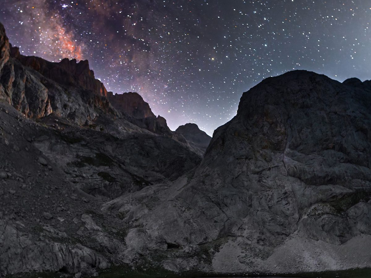 The Milky Way over a tent in rocky mountain terrain