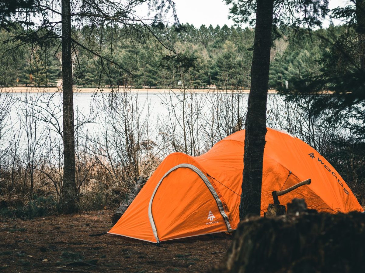 An orange camping tent pitched near a serene lake