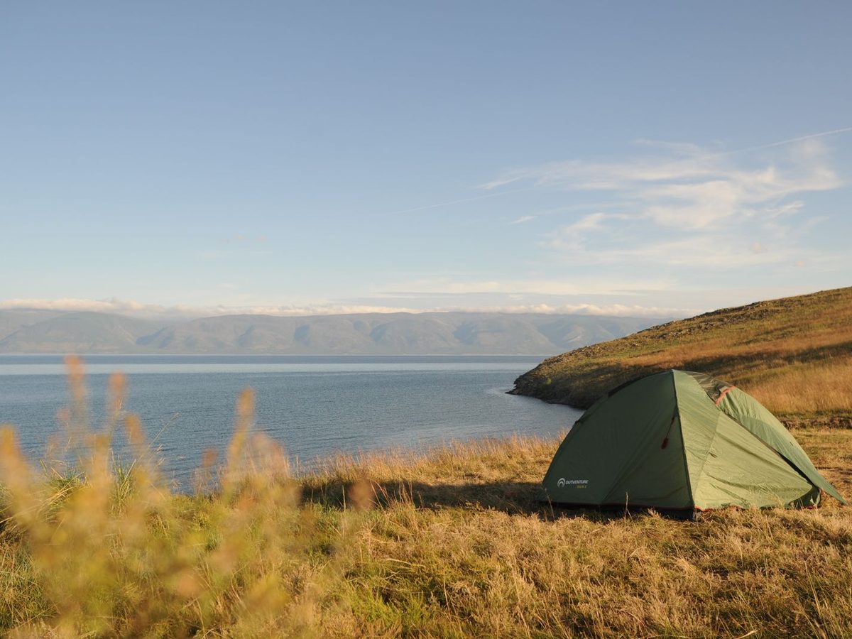 A green tent pitched on a grass field near water at a drive-up campsite
