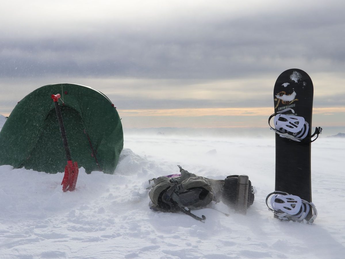 A tent, shovel, and backpack staged in deep snow — winter camp