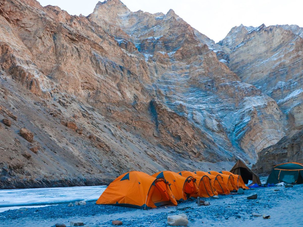 A row of bright orange expedition tents on rocky ground beneath high peaks