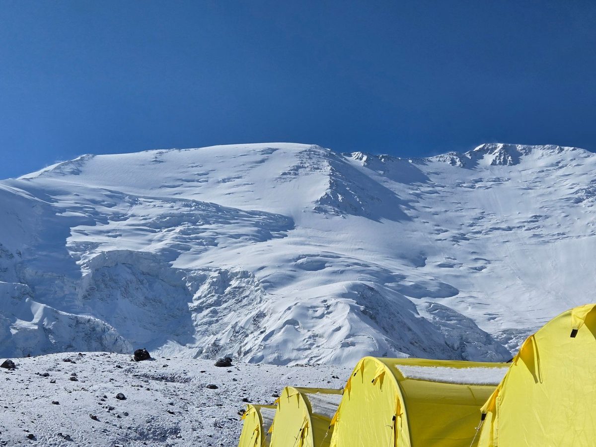 Bright yellow expedition tents on a snowy mountain under a clear sky