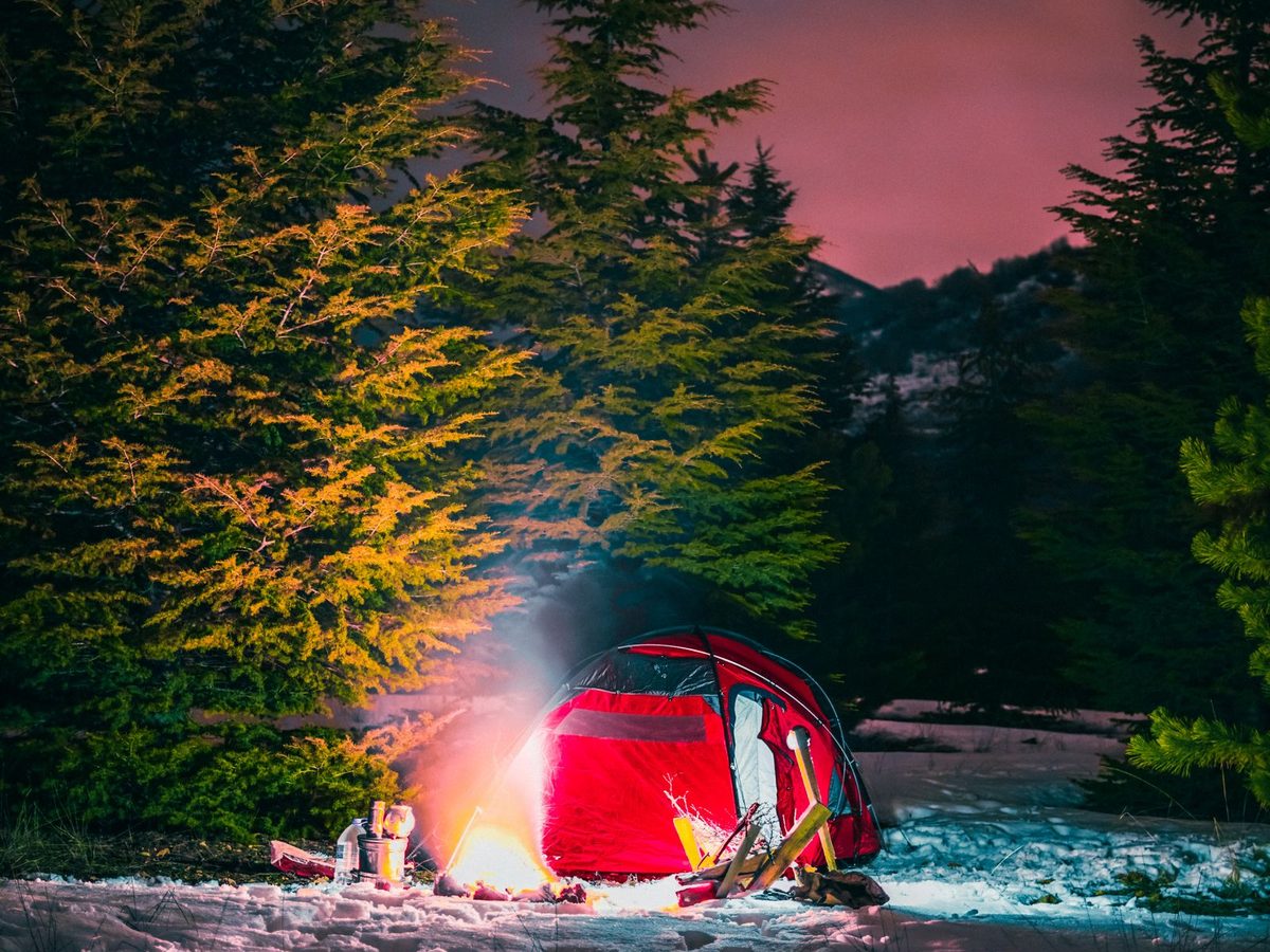 A red tent and a glowing campfire in snowy woods at dawn